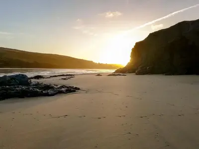 a beach with the sun setting between two cliffs at Trevone in St Merryn