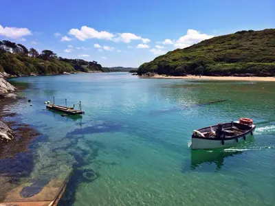 two boats are docked in the water near a beach at Rawley point in Newquay