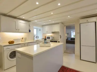 a kitchen with white cabinets and a washer and dryer at Little Barn Cottage in Portloe