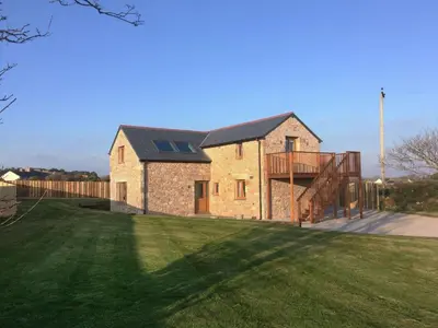 a brick house with a black roof and a yard at The Hayloft in Breage