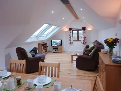 a living room with couches and a table and a tv at The Hayloft in Breage