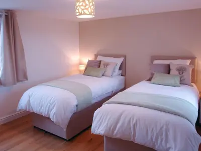 two beds in a room with white walls and wood floors at The Hayloft in Breage