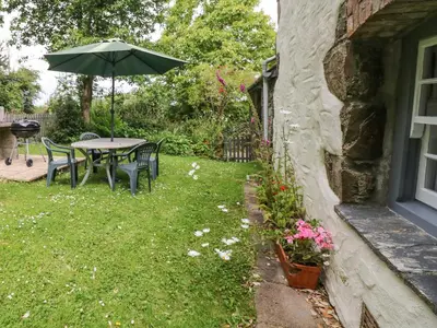 a table and chairs with an umbrella in a yard at Badger Cottage in Mawgan