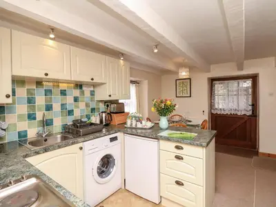 a kitchen with white cabinets and a washer and dryer at Swift Cottage in Mawgan