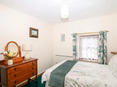 a bedroom with a bed and a dresser and a window at Swift Cottage in Mawgan