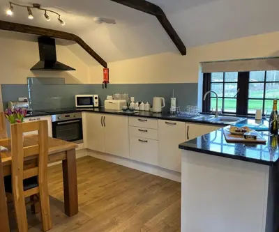 a large kitchen with white cabinets and a table at Maple & Beech Barns in Truro