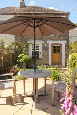 a table with an umbrella in front of a house at Sky Cottage in Golant village near Fowey in Fowey