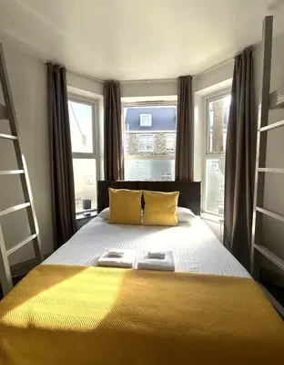 a bedroom with a large bed with yellow sheets and windows at Town Lodge in Newquay