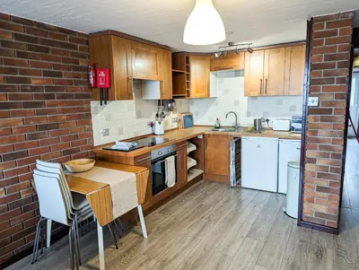 a kitchen with wooden cabinets and a brick wall at South Fistral View Apartment in Newquay