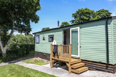 a green holiday home with a wooden deck at Tehidy Holiday Park in Illogan