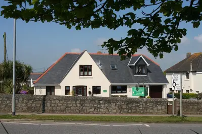 a white house with a gray roof and a stone wall at Mandeley Guest House in Helston