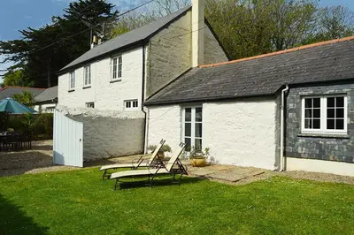 a house with two chairs and a table in a yard at Mews Cottage in Cury