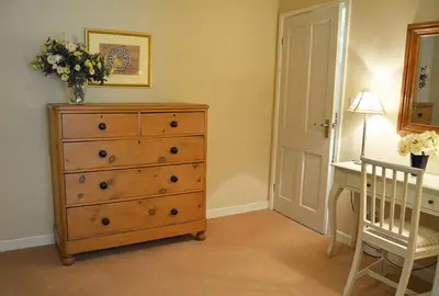 a bedroom with a dresser and a desk with a vase of flowers at St Corantyn Cottage in Helston