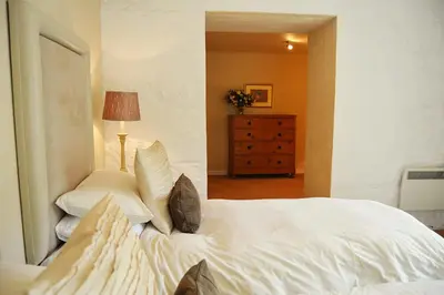a bedroom with a white bed and a dresser with a lamp at St Corantyn Cottage in Helston