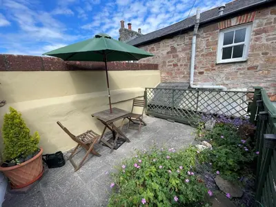 a patio with two chairs and a green umbrella at Ivy Cottage, in Lostwithiel