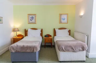 two beds in a room with two tables and two lamps at Tyacks Hotel in Camborne