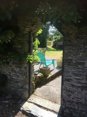 a green bench sitting in a garden through an archway at Polean Farm Old Farmhouse - With Large Jacuzzi, Games Room, Near the Sea and with Free Access to a Nearby Pool in Looe
