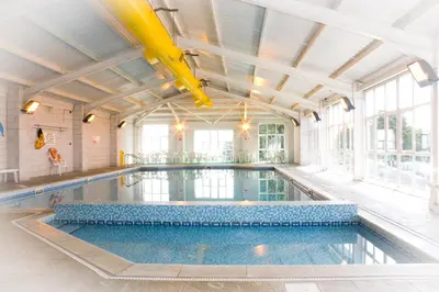 an indoor swimming pool with a large ceiling at Polean Farm Old Farmhouse - With Large Jacuzzi, Games Room, Near the Sea and with Free Access to a Nearby Pool in Looe