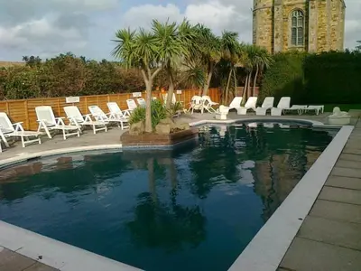 a swimming pool with chairs and palm trees and a building at Priory Lodge Hotel in Newquay