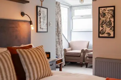 a bedroom with a bed and a chair and a window at Port Gaverne Hotel in Port Isaac