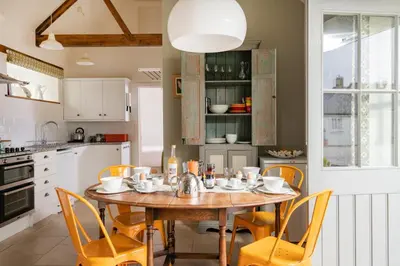 a kitchen with a wooden table and yellow chairs at Lambriggan Court in Perranzabuloe