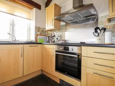a kitchen with wooden cabinets and a black oven at Wheal Kitty in Newlyn East