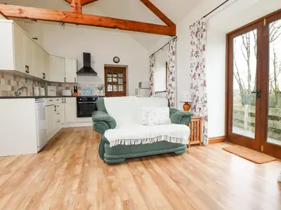 a living room with a green chair and a kitchen at Brocks Barn in Lanlivery
