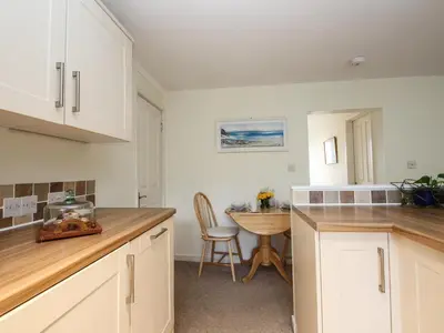a kitchen with white cabinets and a table with a chair at An Kres in Mevagissey