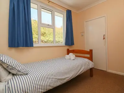 a bedroom with a bed with blue curtains and a window at The Shack in Mawgan Porth