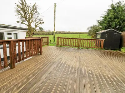 a wooden deck with a fence and a house at Trelydarth in St. Agnes