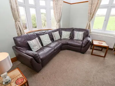 a brown leather couch in a living room with windows at Trelydarth in St. Agnes