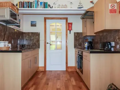a kitchen with wooden cabinets and a white door at Summerfield Cottage in Gorran Haven