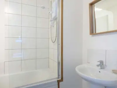 a white bathroom with a shower and a sink at Tidewood in Polzeath
