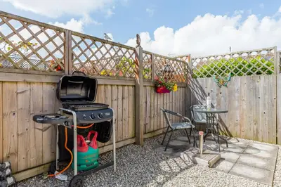 a backyard with a fence and a grill and a table at 19 Cormorant Drive The Annexe in St Austell