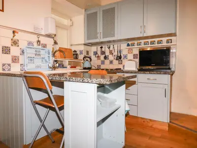 a kitchen with white cabinets and a counter with a chair at The Ark Cottage in Par