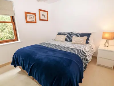 a bedroom with a bed with a blue blanket and a window at The Creekside in Looe
