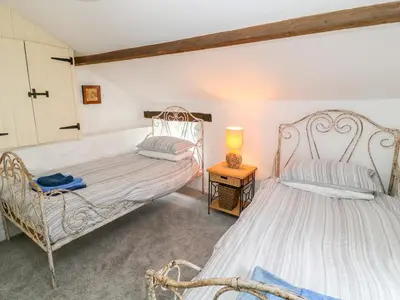a bedroom with two beds and a table with a lamp at Treverbyn Smithy in Saint Neot