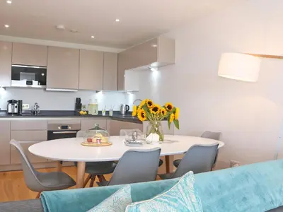 a white kitchen with a white table and chairs at Saltwater, One Lusty Glaze in Newquay