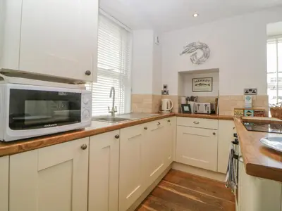 a kitchen with white cabinets and a microwave at Curlews Cottage in Looe