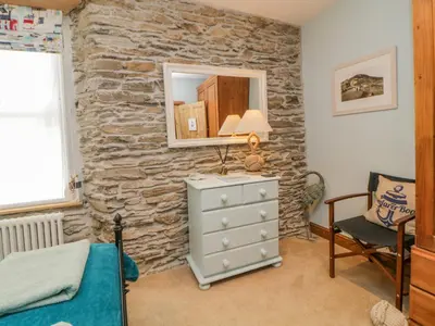 a bedroom with a stone wall with a dresser and a mirror at Curlews Cottage in Looe