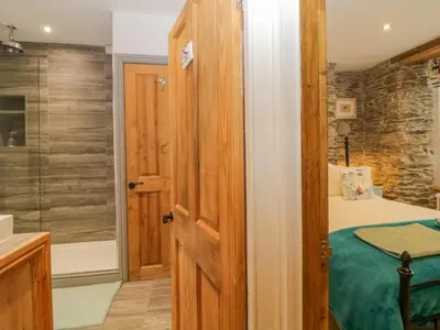 a bathroom with a bed and a glass shower at Curlews Cottage in Looe