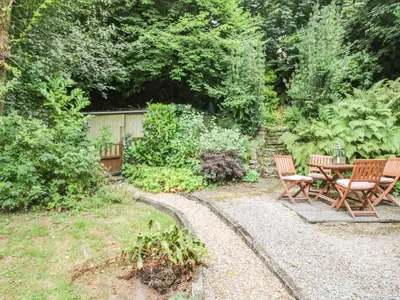 a patio with two chairs and a table in a garden at Tinners Cottage in Saint Cleer
