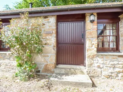 a stone house with a wooden door and a tree at Flower House in Saint Erth