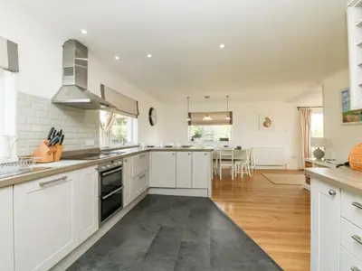 a kitchen with white cabinets and a dining room at Seaport Lodge in Mawgan Porth