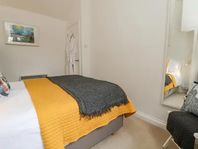 a bedroom with a bed with a yellow blanket and a mirror at Mackerel Sky in Marazion