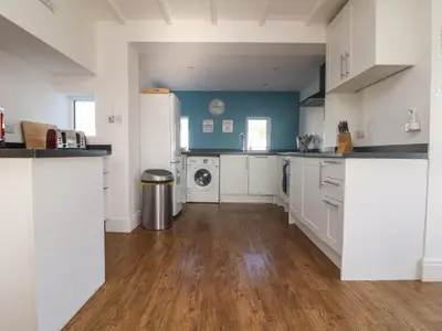 a kitchen with white cabinets and a washer and dryer at Gwillen in Mawgan Porth
