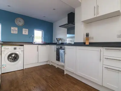 a kitchen with white cabinets and a washer and dryer at Gwillen in Mawgan Porth