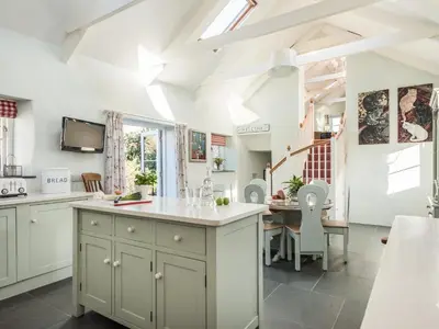 a kitchen with white cabinets and a dining room with a table at The Barn at Little Resugga in Bugle