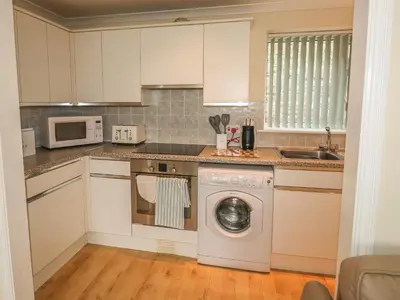 a kitchen with white cabinets and a washing machine at Kingfisher House in Tintagel