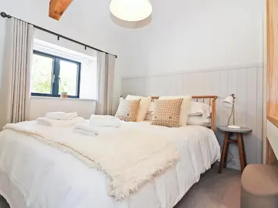 a white bedroom with a large bed with white sheets and pillows at Long House, Boskensoe Barns in Helford Passage